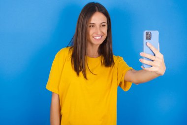 Mutlu ve güzel genç bir kadının izole edilmiş çekimi, cep telefonuyla selfie çekiyor. İnsanlar, teknoloji ve eğlence kavramı