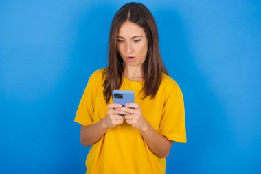 Güzel, genç bir kadın meraklı gözlerle bakıyor, modern akıllı telefonu tutuyor, arkadaşından beklenmedik bir mesaj alıyor,.