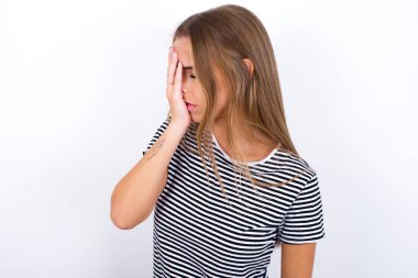 Güzel sarışın kız beyaz arka planda çizgili tişört giyiyor ve ağlarken suratını ellerle kapatıyor. Depresyon kavramı.