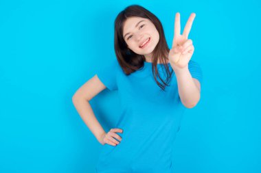 Mavi tişört giyen genç beyaz kız mavi stüdyo arka planında izole edilmiş parmaklarını kameraya çevirir ve birini seçer. Seni tavsiye ederim. En iyi seçim