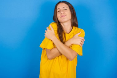 Güzel genç bir kadın mutlu ve olumlu bir şekilde kendine sarılıyor, kendinden emin gülümsüyor. Sevgi ve özgüven..