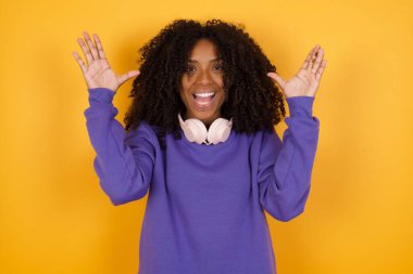 Sarı arka planda kulaklıkları olan Afro-Amerikan bir kadının portresi.