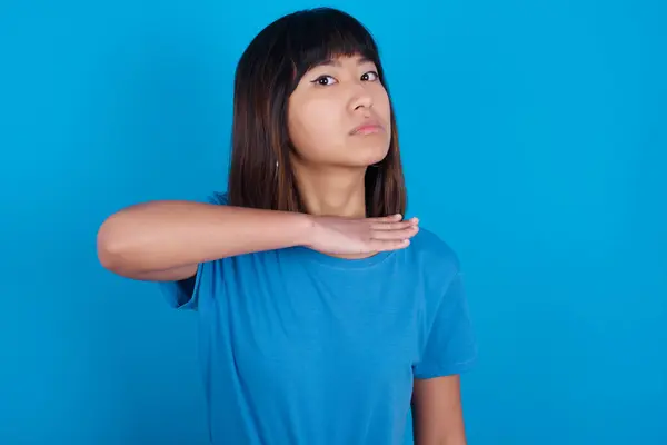 青い背景に青いTシャツを着た若いアジアの女性は ナイフとして手で喉を切断し 激しい暴力で攻撃を脅かします — ストック写真