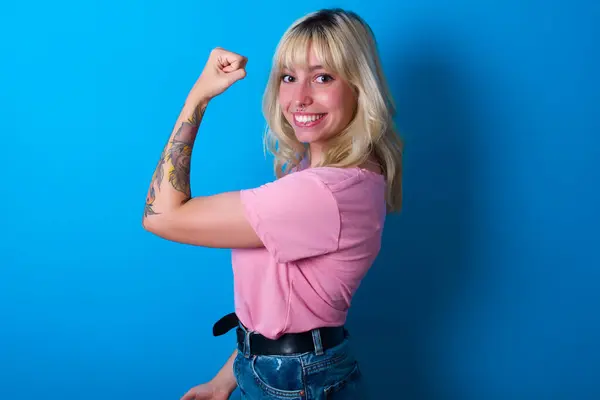 穿着粉色T恤的高加索女孩在运动后被隔离在蓝色背景下 显示出肌肉 健康和力量概念 — 图库照片