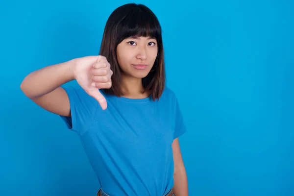 Młoda Azjatycka Kobieta Niebieskiej Koszulce Niebieskim Tle Wygląda Nieszczęśliwie Wściekle — Zdjęcie stockowe