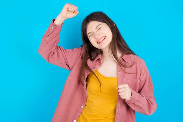 迷人的年轻高加索女孩穿着粉色衬衫 与蓝色背景隔离 用拳头和灿烂的笑容庆祝胜利 — 图库照片