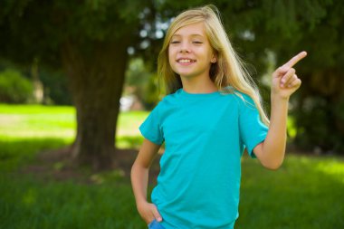 Olumlu ifadeli güzel bir kız, her iki işaret parmağıyla işaret ediyor, geniş bir gülümsemesi var. Şuraya bakın, lütfen..