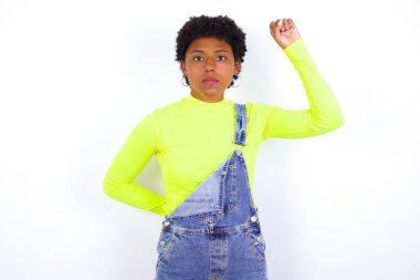 Beyaz duvara karşı kot pantolon giyen genç Afrikalı Amerikalı kadın ciddi, güçlü ve isyankar hissediyor, yumruğunu kaldırıyor, protesto ediyor veya devrim için savaşıyor..