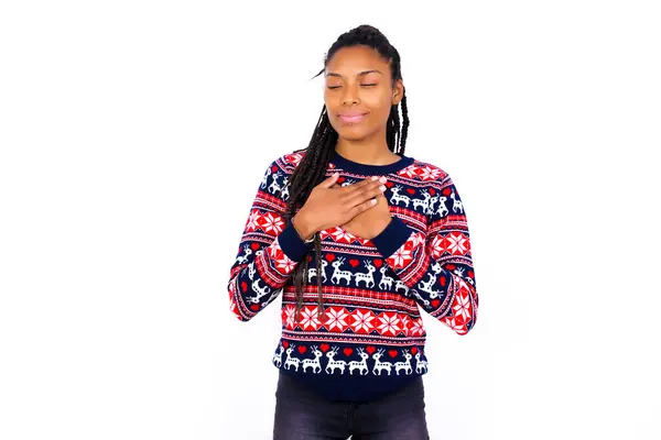 白い壁にクリスマスセーターを着用したアフリカ系アメリカ人女性は目を閉じて胸に手を置き 誠実な感情を表現し 親切で正直である ボディランゲージとリアルな気持ちのコンセプト — ストック写真