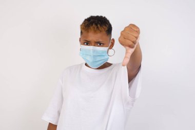 Hoşnutsuz genç Afro-Amerikan kadın beyaz tişört giyiyor, onaylamadığını gösteriyor, başparmağını aşağıda tutuyor, hoşnutsuzluğunu ifade ediyor, hoşnutsuzluğunu ifade ediyor, beyaz gömlek giyiyor, gri arka plan üzerinde izole edilmiş. Vücut dili kavramı.