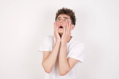 Beyaz arka plandaki yakışıklı genç adam ellerini yanaklarından ayırmıyor ve sıkılmış bir ifade var. Stresli umutsuz model