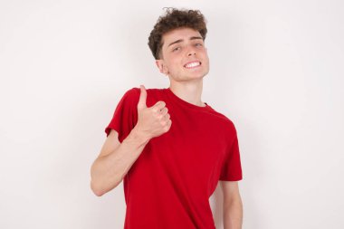 Beyaz arka plandaki yakışıklı genç adam baş parmağını kaldırıyor, aferin! Olumlu insani duygu yüz ifadesi vücut dili.