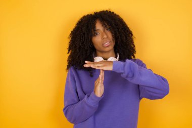 Sarı arka planda kulaklıklı Afro-Amerikalı genç bir kadının portresi.