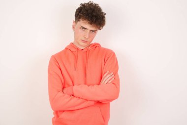 Beyaz arka planda yakışıklı genç bir adam hoşnutsuzca kaşlarını çatıyor, kollarını kavuşturup, bir açıklama bekliyor..