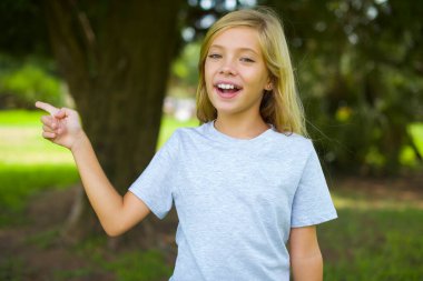 Beyaz tişörtlü beyaz bir kız açık havada durup gülüyor boş bir alanda mutlu bir şekilde işaret ediyor. İyi haber ya da beklenmedik satıştan etkilenmiş, indirimli alışveriş yapıyor..