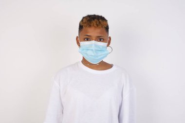 Beyaz tişört giyen, kameraya bakan, düşünen ya da merak eden neşeli Afro-Amerikan kadının belden yukarı pozu. İki kolunu da indir, tarafsız yüz ifadesi..