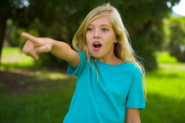 Parkta dikilip parmağıyla işaret eden mavi tişörtlü güzel beyaz bir kızın portresi.