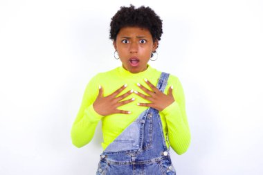 Beyazlara karşı kot pantolon giyen genç Afrikalı Amerikalı kadın ellerini göğsünde tutuyor şok olmuş ve korkmuş hissediyor, ağzı açık kameraya bakıyor ve diyor ki:?