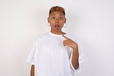 Beyaz tişört giyen afro-amerikalı güzel bir kadının sersemlemiş bir şekilde kendini parmağıyla göstererek 