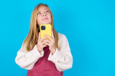 Hayalperest bakışlı, akıllı telefonu tutarken düşünen güzel bir genç kızın portresi. Bir mesaj yazmaya çalışır.