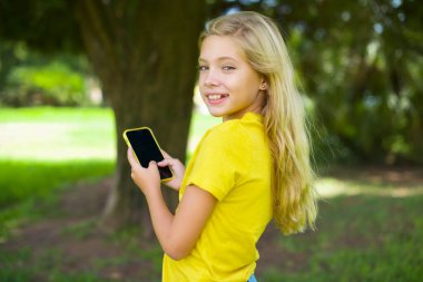 Kafkasyalı küçük bir kızın arka plan fotoğrafı. Sarı tişört giymiş, akıllı telefondan gülümsüyor.
