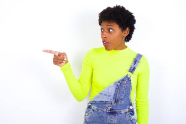 Kısa saçlı afro-amerikalı afro-amerikan bir kadın, beyaza karşı kot pantolon giyiyor ve çok şaşırmış bir ifadeyle fotokopi çekiliyor.