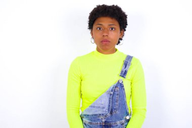 Neşeli genç bir kadın kameraya bakıyor, bir şey düşünüyor. İki kolunu da indir, tarafsız yüz ifadesi..