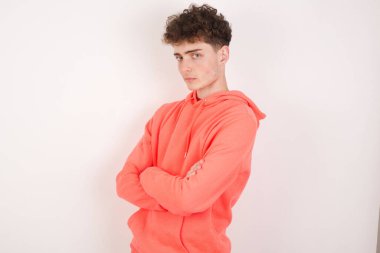 Beyaz arka planda kolları bağlı neşeli, yakışıklı bir genç adam resmi. Kameraya bakıp gülümsüyor. Güven kavramı.