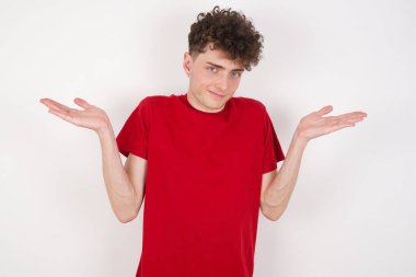 Belki evet ya da hayır. Beyaz arka plandaki şüpheli yakışıklı genç adam şaşkınlık içinde omuz silkiyor, ne istediğine karar vermeye çalışıyor. Tereddüt ve belirsizlik.