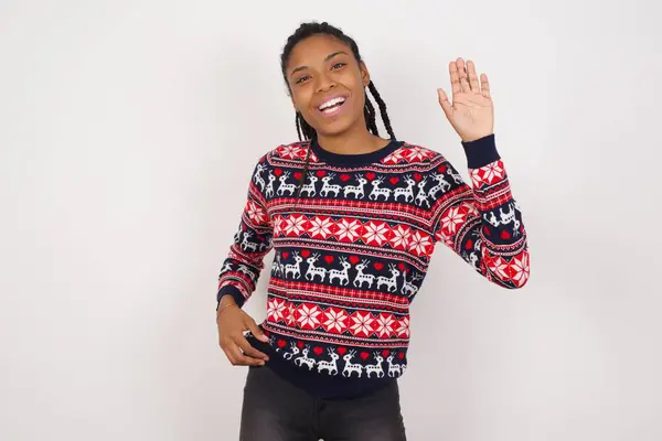 身穿圣诞毛衣 靠着白墙的非洲裔美国女人放弃说声 开心地微笑着 友好地欢迎他人 — 图库照片
