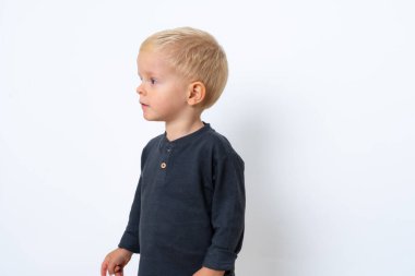 Stüdyoda, beyaz stüdyo arka planında siyah tişört ve beyaz pantolon giyen mutlu sarışın çocuğun fotoğrafı.