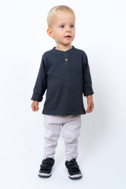 Stüdyoda, beyaz stüdyo arka planında siyah tişört ve beyaz pantolon giyen mutlu sarışın çocuğun fotoğrafı.