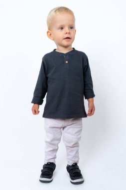 Stüdyoda, beyaz stüdyo arka planında siyah tişört ve beyaz pantolon giyen mutlu sarışın çocuğun fotoğrafı.