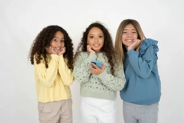 Joyous 3人のティーンエイジャーの女の子は 携帯電話デバイスでポーズし 現代のスマートフォンにテキストメッセージを入力し 自由時間中に面白いビデオを見て 良いインターネット接続を楽しんでいます — ストック写真