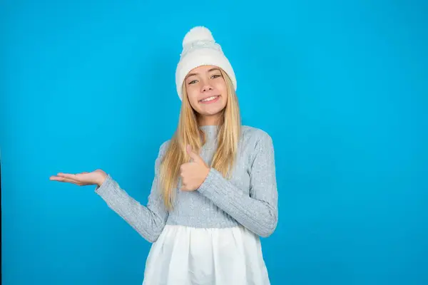 Schöne Junge Mädchen Mit Weißer Strickmütze Und Blauem Pullover Zeigt — Stockfoto