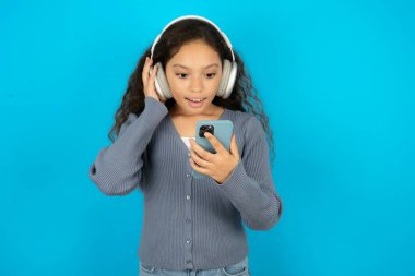 Gri kazak giyen mutlu genç kız akıllı telefon ekranında odaklanırken kendini iyi hissediyor. İnsanlar, teknoloji, yaşam tarzı