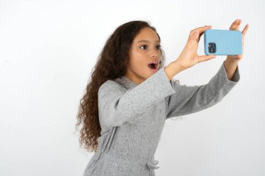 Gri kazak giyen genç bir kız sosyal medyaya göndermek için selfie çekiyor ya da arkadaşlarıyla görüntülü görüşme yapıyor..