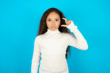 Beyaz kazak giyen genç kız dudak ve el hareketleriyle çok küçük bir şey gösteriyor..