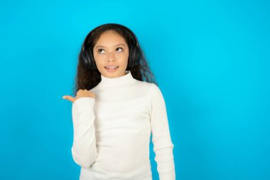 Beyaz kazak giyen genç kız kablosuz kulaklıkla ses kaydı dinliyor.