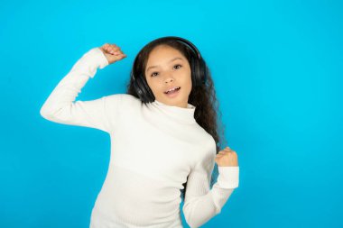 Kaygısız genç kız dişlek tebessümlü beyaz kazak giyiyor. Kollarını kaldırıyor, dans ediyor. Müziğin ritmiyle, müzik listesinden kulaklıkla müzik dinliyor.