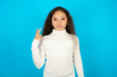 Beyaz kazak giyen genç kız barış jesti yapıyor. Dudaklarını katlanmış V işaretini tutuyor. Vücut dili kavramı