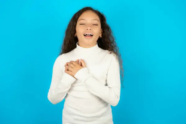 stock image teenager girl wearing white sweater expresses happiness, laughs pleasantly, keeps hands on heart