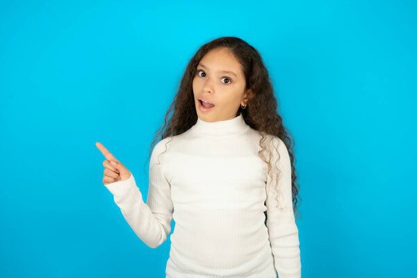 Emotive teenager girl wearing white sweater keeps jaw dropped from shock demonstrates amazing promo points right on blank space demonstrates big shopping sale. Advertisement