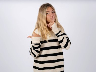 Beyaz arka planda çizgili örgü süveter giyen Kafkas ergen bir kız sessiz olup dudaklarını yana doğru gösteren parmaklarıyla sessiz olmasını istiyor. Sessizlik ve gizli konsept.