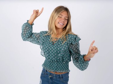 Beyaz atölyenin arka planında yeşil şifon bluz giyen neşeli beyaz bir kızın fotoğrafı eğlenceli ve tasasız bir şekilde dans ediyor. Mükemmel hareketler yapıyor. Disko partisinde boş zaman geçirir