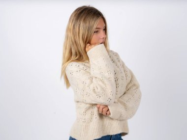 Astonished caucasian teen girl wearing white knitted sweater over white studio background looks aside surprisingly with opened mouth. clipart