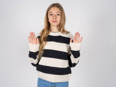 Beyaz stüdyo arka planında çizgili süveter giyen güzel bir genç kız avuç içlerini kameraya çekiyor, jestleri durduruyor, duygularını kontrol etmek ve gergin olmamak istiyor.