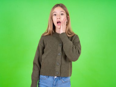 Şok olmuş, beyaz, yeşil kazak giyen güzel bir kız çok şaşırmış görünüyor. Beklenmedik haberler, yüz ifadeleri konseptiyle şaşkına dönüyor..