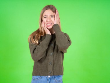 Kederli, umutsuz, ağlayan, yeşil kazak giyen güzel beyaz kız stresli görünüyor, kaşlarını çatıyor, yalnız ve endişeli hissediyor.