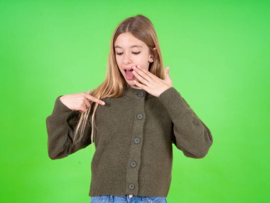 Şok olmuş, beyaz, yeşil kazak giyen güzel bir kız. Şaşırtıcı bir şekilde aşağı bakıyor. Ön parmağıyla boş gösteriyor.